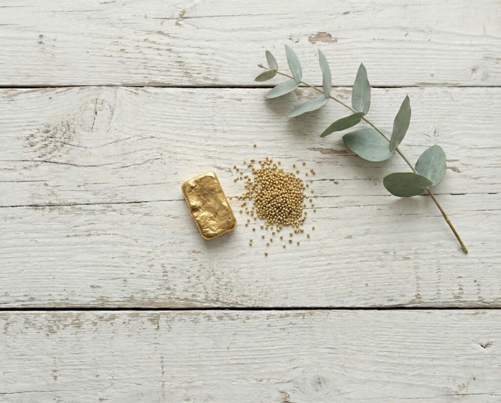 Gold bar, gold granules, and a eucalyptus branch on a wooden background