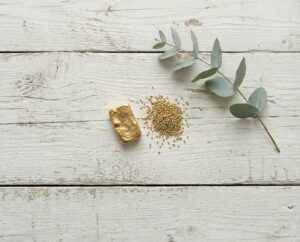 Gold bar, gold granules, and a eucalyptus branch on a wooden background