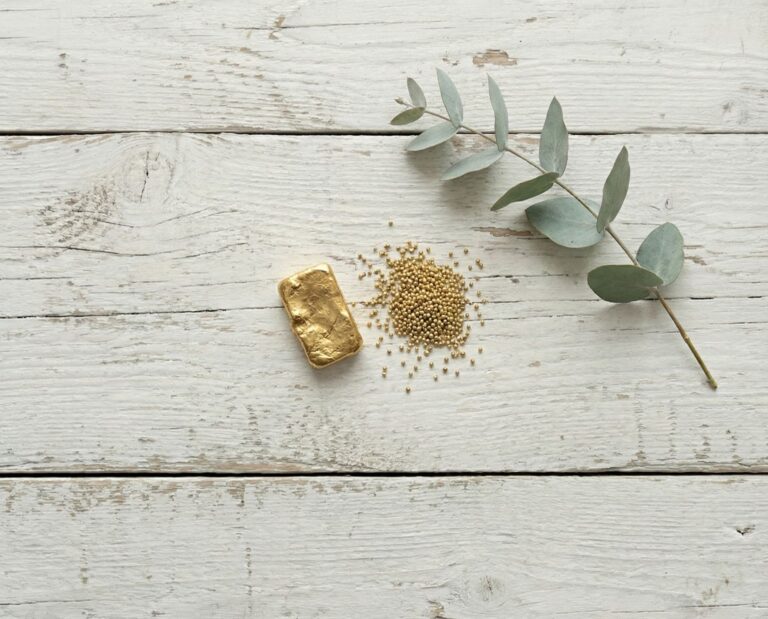 Gold bar, gold granules, and a eucalyptus branch on a wooden background